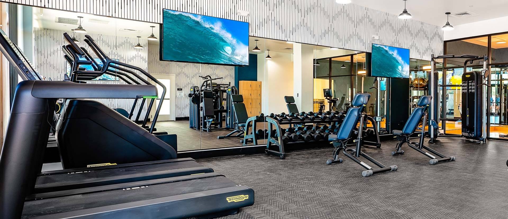 A fitness center equipped with weights, benches, treadmills, a staircase machine, and two flat-screen televisions for entertainment.